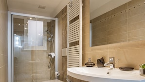 A modern bathroom with a glass shower enclosure, a large mirror, and a curved vanity with a sink and towel rack.