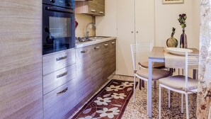 A modern kitchen with wooden cabinets, a built-in oven, and a dining area with a table and chairs.