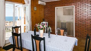 Un coin repas avec une table dressée pour deux personnes, un vase rempli de fleurs et une vue sur la mer par une porte ouverte.