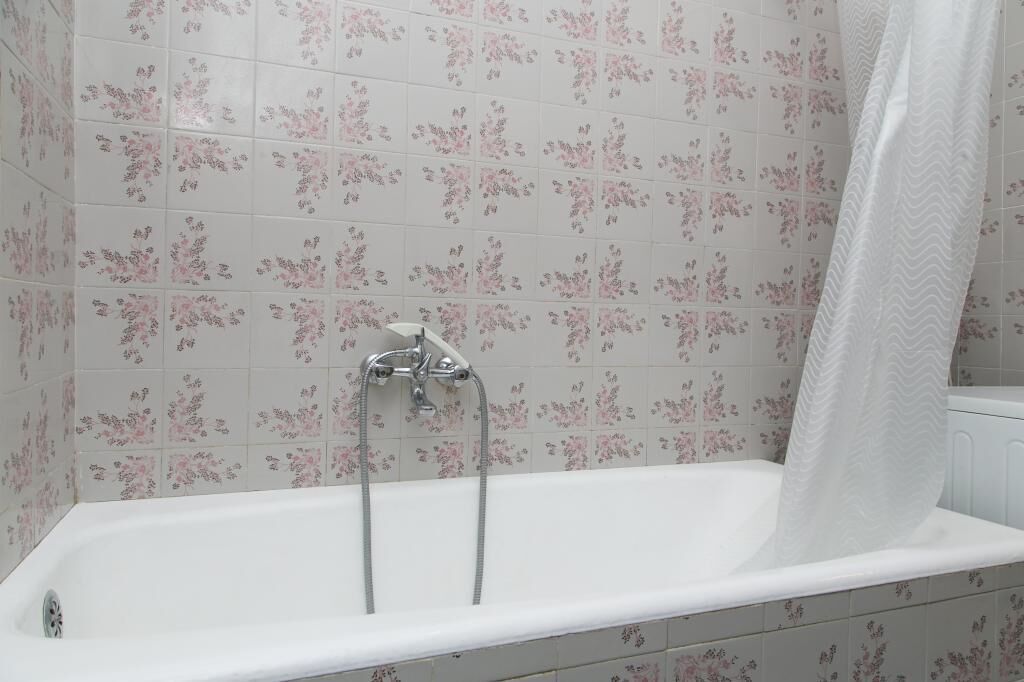 A bathroom with a white bathtub, a shower curtain, and floral-patterned tiles on the walls.