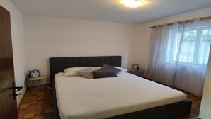 Une chambre à coucher avec un grand lit, une table de chevet, une chaise et une fenêtre avec des rideaux.