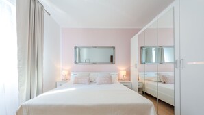 A bedroom with a large bed, two bedside tables with lamps, a mirror above the bed, and a wardrobe.