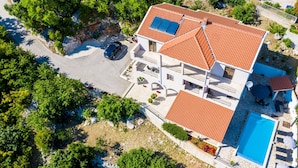 A two-story house with a swimming pool, solar panels, and a car parked in the driveway.