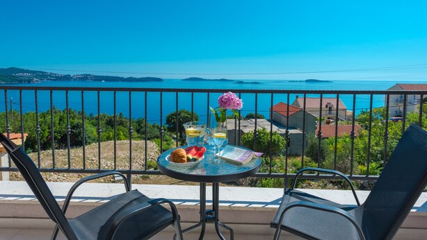 A balcony with a table set for breakfast, overlooking a coastal view.