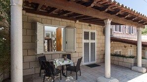 An outdoor patio with a table and chairs, a pergola, and a view of the interior through a window. - Apartments Dia - Studio apartment (Dubrovnik)