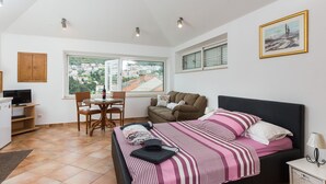 A bedroom with a bed, a desk, a chair, a window with a city view, and a television. - Apartments Dia - Studio apartment (Dubrovnik)
