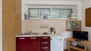 A compact kitchen with wooden cabinets, a sink, a stove, and a small refrigerator. - Apartments Dia - Studio apartment (Dubrovnik)