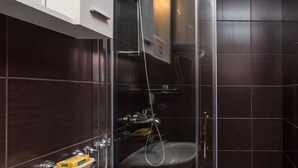 A modern bathroom with a glass shower enclosure, a white sink, and dark tiled walls. - Apartments Dia - Studio apartment (Dubrovnik)