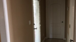 Un pasillo con paredes color beige, una puerta blanca y una ventana con persianas.