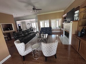 A spacious living room with a black leather sofa, patterned armchairs, a coffee table, and a fireplace.