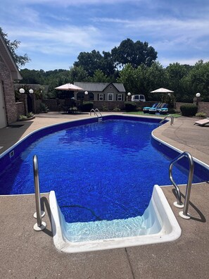 Ein Swimmingpool mit klarem, blauem Wasser, umgeben von einer Terrasse mit Liegestühlen und Sonnenschirmen.