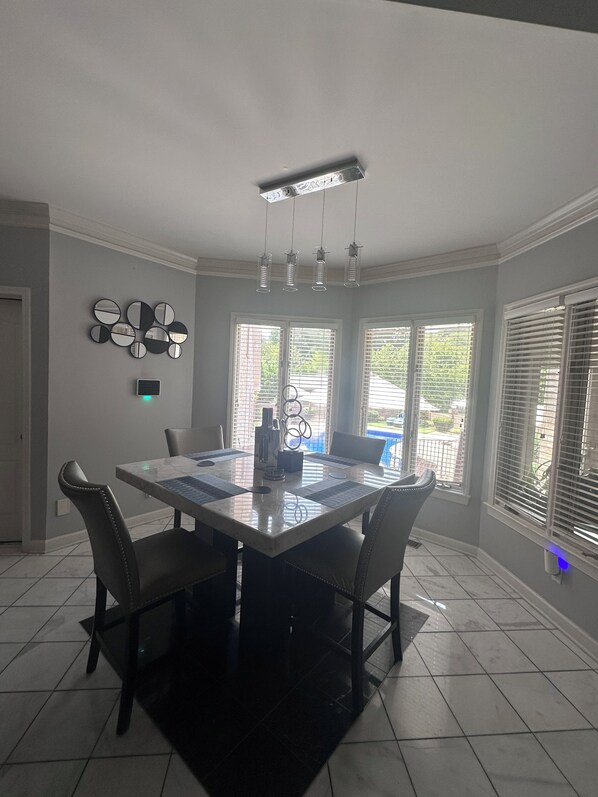 A dining area with a rectangular table, four chairs, a black rug, and a ceiling light fixture.