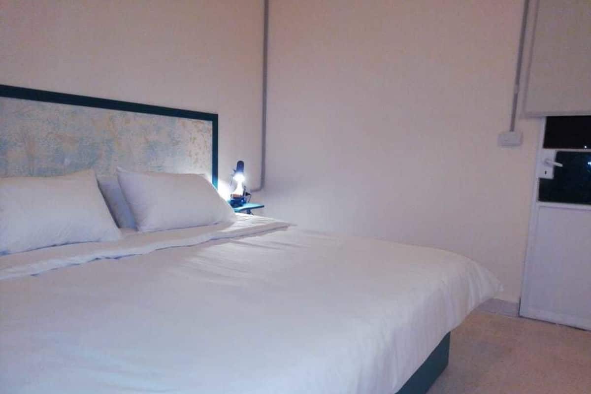 A neatly made bed in a room with a simple headboard and a small bedside table with a lamp.