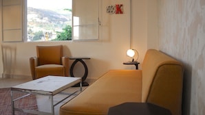 Una habitación con sofá, una mesa y una lámpara. Se ve una ventana con vistas al paisaje.