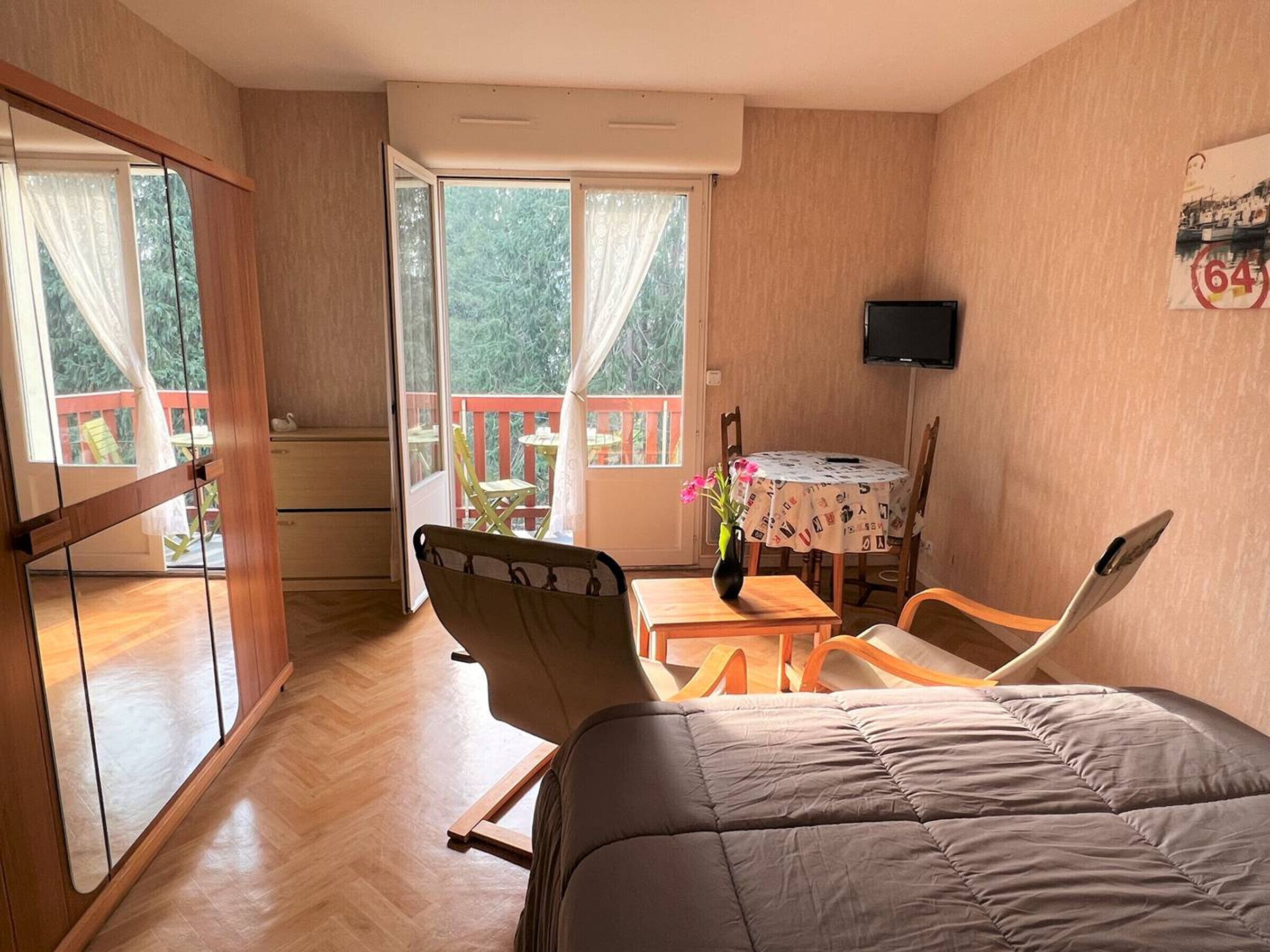 A room with a bed, a desk, a chair, a TV, and a balcony with a table and chairs.