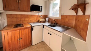 Una cocina compacta con armarios de madera, un microondas, un lavamanos y un ventanal.