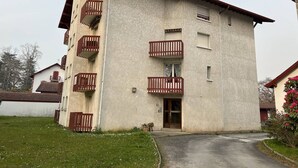 Un edificio de varios pisos con balcones, una entrada central y un pequeño jardín.