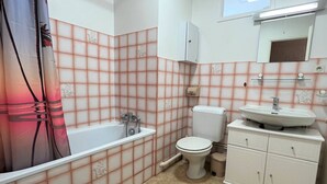 Un baño con bañera, inodoro, lavabo y un espejo sobre el lavabo.