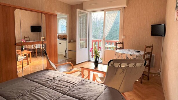 Un dormitorio con cama, escritorio, silla, televisor y balcón con vistas a árboles.