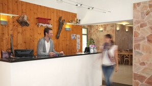 A reception area with a wooden wall, a reception desk, and a stone wall in the background. - Residence Val de Roland - Studio Apartment 2 persons (Luz-Saint-Sauveur)