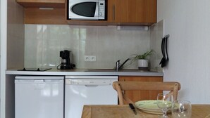 A compact kitchen with wooden cabinets, a microwave, a dishwasher, and a dining table set with plates and cutlery. - Residence Val de Roland - Studio Apartment 2 persons (Luz-Saint-Sauveur)