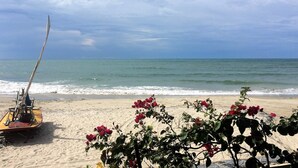 A sandy beach with a boat and red flowers in the foreground. - Villa Isola Bella (Fortim)
