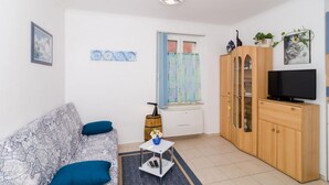 Ein Wohnzimmer mit einer Couch, einem Fernseher, einem Schrank und einem Fenster mit Vorhängen.