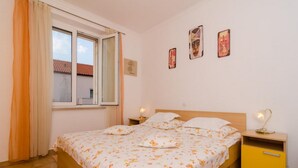Ein Schlafzimmer mit einem Bett, zwei Nachttischen, einem fensterbelaubten Fenster und drei gerahmten Bildern an der Wand.
