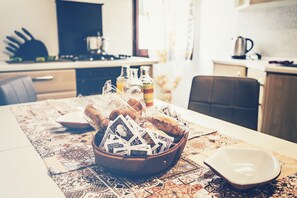 Une table à manger avec un panier de pain et un jeu de cartes, un tapis décoratif et une cafetière en arrière-plan.