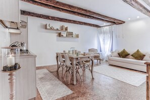 Un salon moderne avec un coin repas, des poutres en bois au plafond et un canapé blanc agrémenté de coussins verts.
