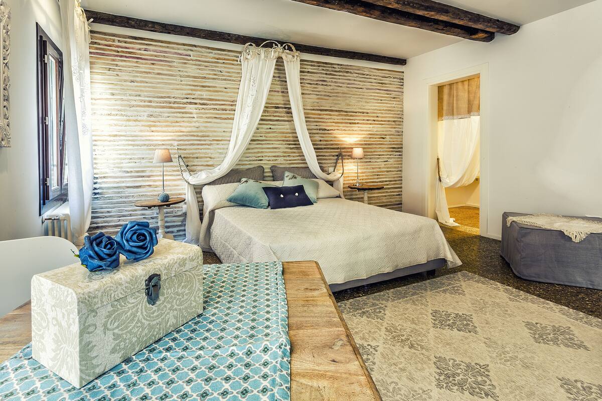Een slaapkamer met een bed, nachtkastjes, een bankje, een dressoir en een kamerbreed tapijt met dessin.
