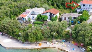 An aerial view of a coastal area with a beach, clear turquoise water, and several buildings with red roofs. - Apartments Vesela - Comfort One Bedroom Apartment with Balcony and Sea View (Janjina)
