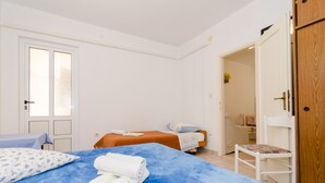 Une chambre d’hôtel avec deux lits, une armoire en bois, une chaise et une salle de bain visible à travers une porte ouverte.