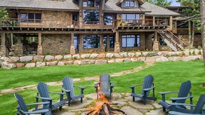 Une grande maison en pierre avec un foyer et des fauteuils Adirondack dans la cour.