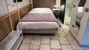 Quarto moderno com cama grande, cabeceira de madeira, mesa de cabeceira pequena, espelho e área de chuveiro.