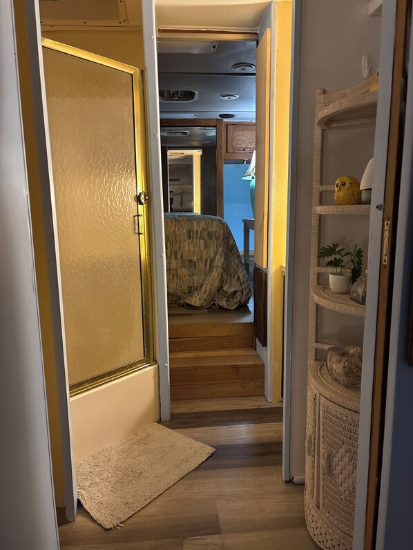 An interior hallway with a wooden door, a carpeted area, and a bed with a patterned cover. - Privacy RV Marsh site. Fantastic location! Very comfortable renovated RV. (Steinhatchee)