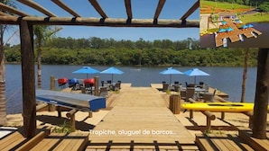 A wooden deck with outdoor seating and umbrellas overlooking a lake. - House with heated pool. Santa Bárbara Resort Residence #casadecampo131 (Águas de Santa Bárbara)