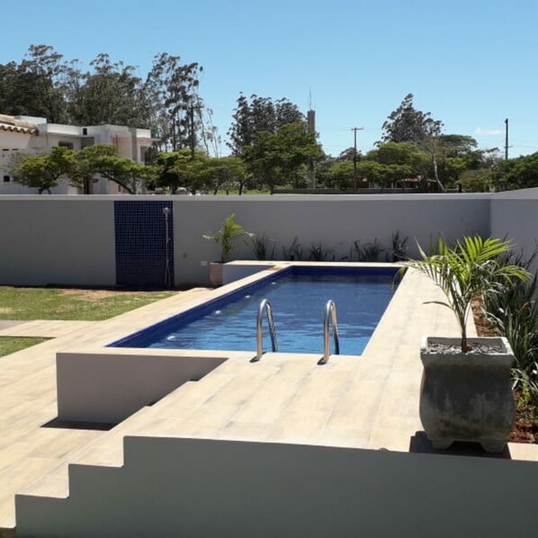 Une piscine rectangulaire dotée de deux échelles en métal, entourée d’une terrasse carrelée de couleur claire.