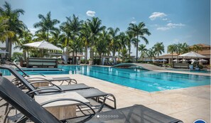 Un espace piscine aménagé avec des chaises longues, des parasols et des palmiers.
