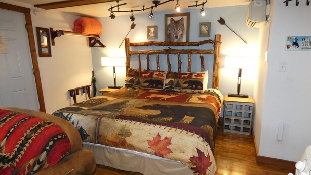 Ein gemütliches Zimmer mit einem Bett, ausgestattet mit einem Bettbezug mit Waldmotiv, einem hölzernen Kopfteil und einer Wandlampe.