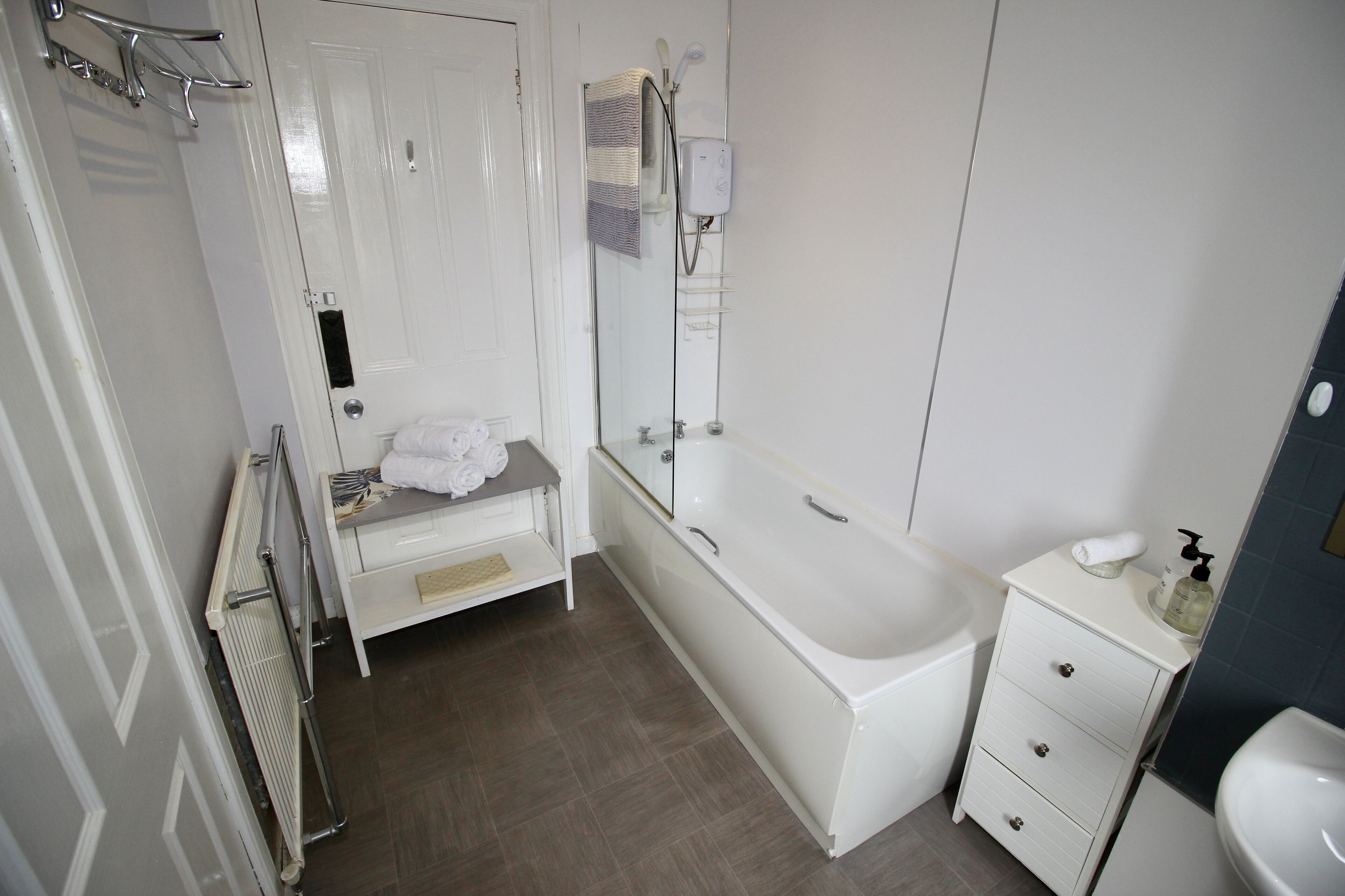 A bathroom with a bathtub, a toilet, a sink, a towel rack, and a shelf with towels.