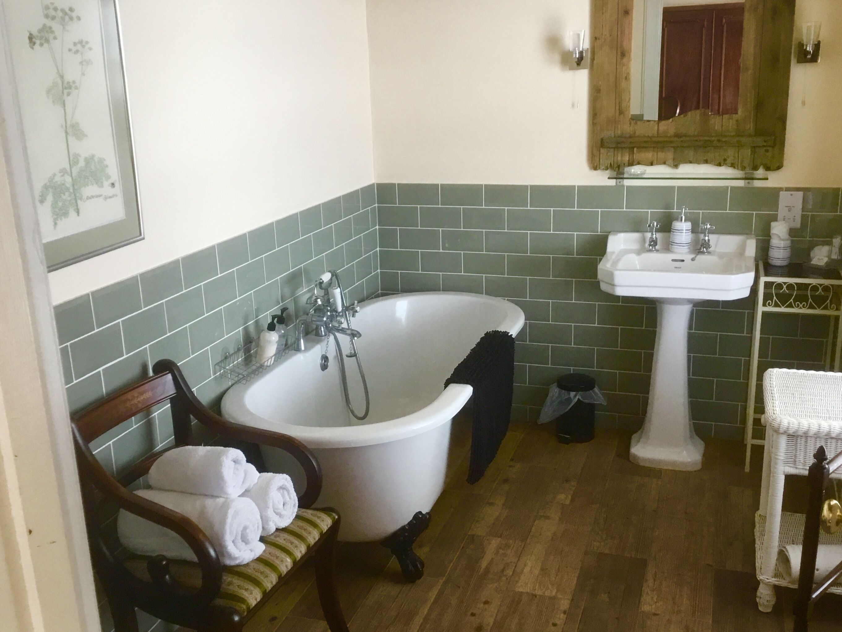Une salle de bain avec une baignoire blanche, un lavabo blanc et une chaise en bois sur laquelle sont posées des serviettes.