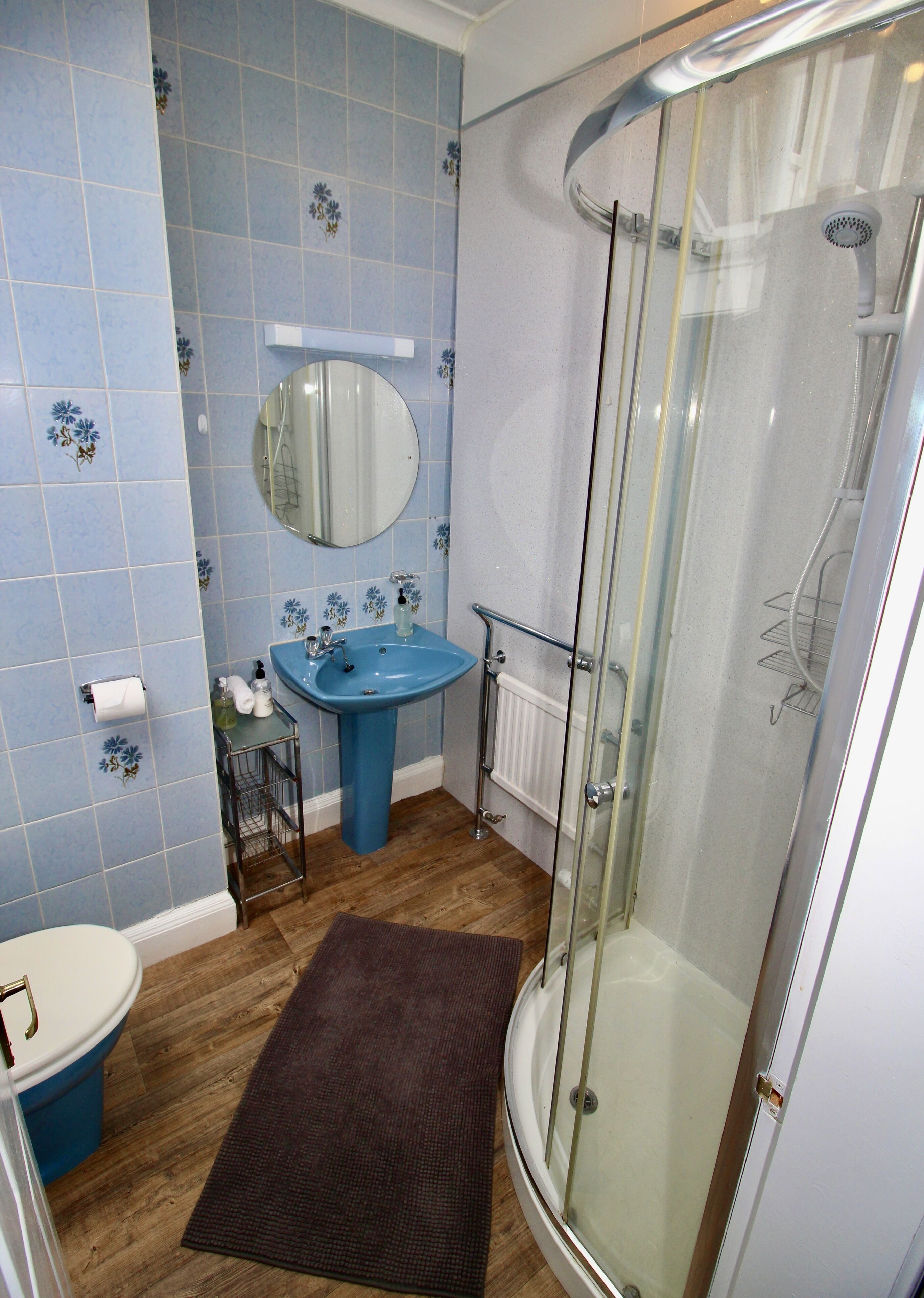 A bathroom with a blue sink, a round mirror, a toilet, and a glass-enclosed shower.