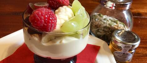 Un dessert composé de framboises, de raisins et de tranches de banane, présenté dans un plat en verre, accompagné d’un pot de miel et d’un récipient de flocons d’avoine.