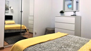 Ein Schlafzimmer mit einem Bett, einem Schminktisch, einem Spiegel und einer kleinen Pflanze.