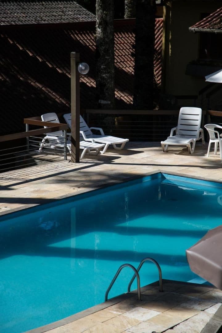 A swimming pool with a metal ladder, surrounded by white lounge chairs and a wooden fence.