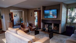 Un salon comprenant un canapé, des fauteuils, une cheminée, un téléviseur diffusant des informations financières et une plante.