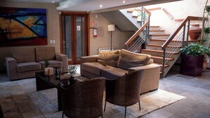 Un salon moderne avec un canapé, deux fauteuils, une table basse et une cheminée. On aperçoit un escalier au fond.