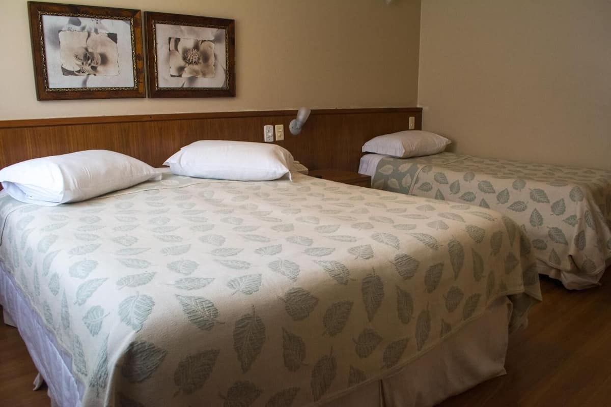 Habitación de hotel con dos camas, cada una con ropa de cama de diseño floral y un cabecero de madera, además de dos cuadros en la pared.