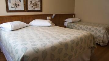 A hotel room with two beds, each with leaf-patterned bedding, a wooden headboard, and two framed pictures on the wall.